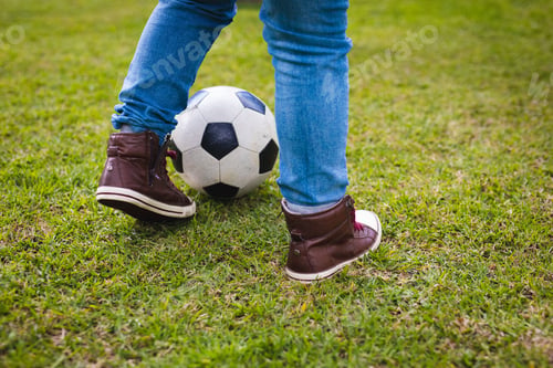 Preview: School-age boy balancing black-and-white soccer ball on grass wearing jeans and sneakers
