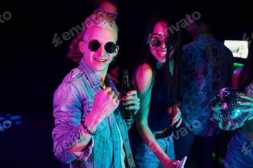 Preview: Hipster guy in sunglasses and with bottle of alcohol posing for camera in front of young people