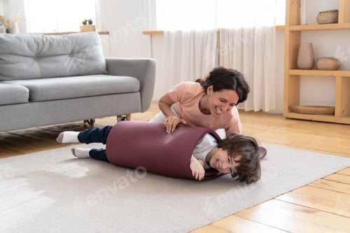 Preview: Mother wrapped smiling kid in yoga mat playing with son after sport exercise at home during lockdown