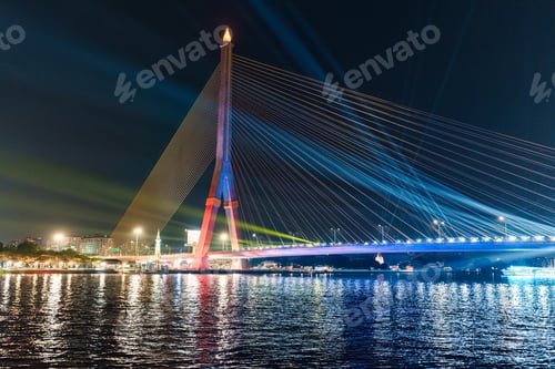 Preview: Colorful night view of suspension bridge with light up reflection on waterfront