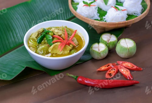 Preview: Chicken green curry in white ceramic bowl with rice noodles on wooden table decorations