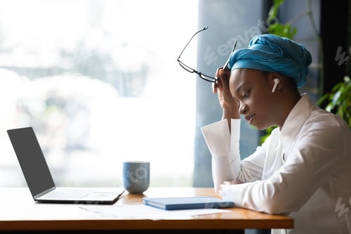 Preview: Exhausted black businesswoman working online, cafe interior, side view