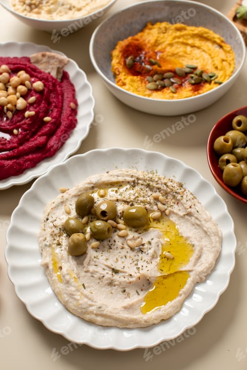 Preview: Different types of hummus in bowls and plates. Beetroot, pumpkin, chickpea and bean hummus.