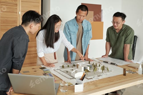 Preview: Young Chinese businesswoman pointing at house layout among colleagues