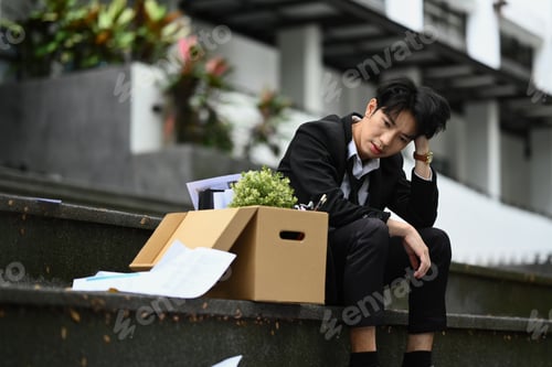 Preview: Upset, frustrated male office worker sitting on stairs outside building.