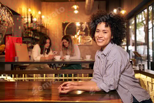 Preview: Cheerful Latin empowered woman curly hair looking at camera. Girlfriends having fun in a bar