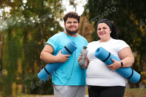 Preview: Overweight couple wearing sportswear with mats in park