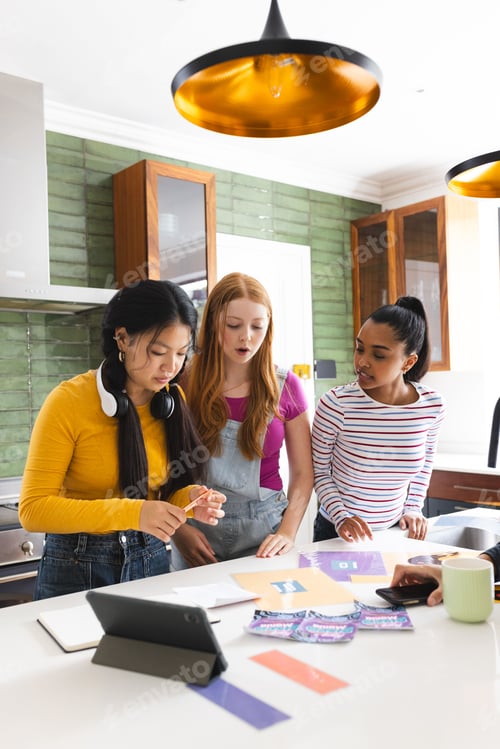 Preview: In kitchen, teen girls using tablet and colorful papers for creative project