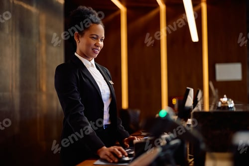Preview: Black female concierge using computer while working at hotel reception.