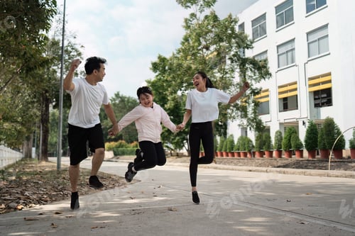 Preview: Happy Family Jumping Together Outdoors in Casual Clothing Near Modern Building on a Sunny Day