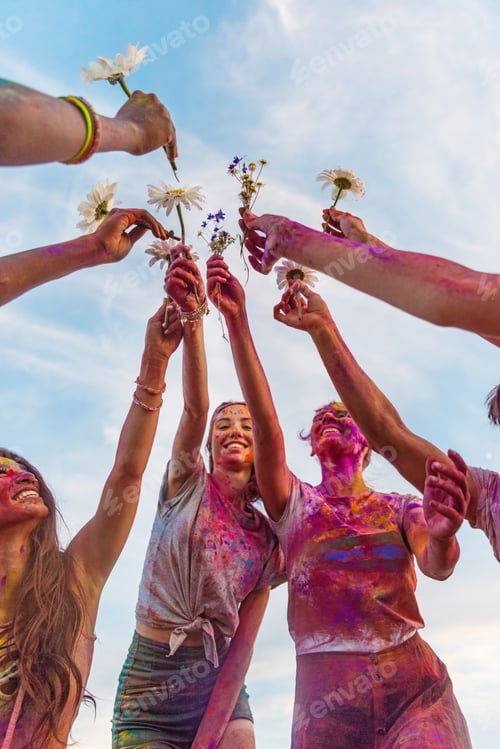 Preview: cheerful young friends with colorful paint on clothes holding chamomiles at holi festival