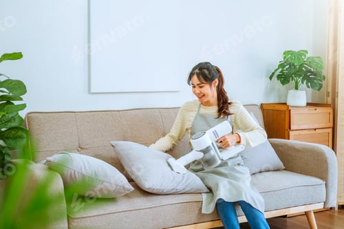 Preview: Young Woman Vacuuming Pillows on Couch at Home