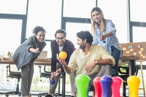 Preview: Businessman holding bowling ball near smiling interracial colleagues in office