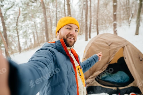 Preview: Man recording winter camping vlog near tent in snowy forest