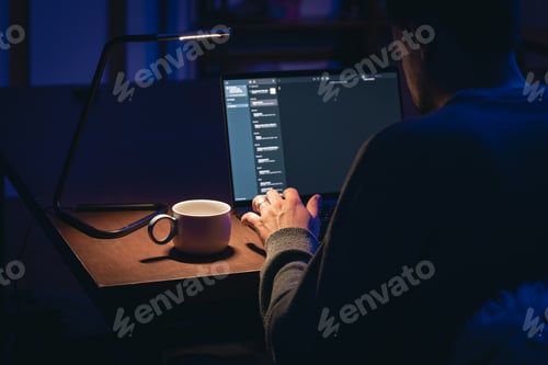 Preview: A man works on a laptop at night, sitting at a table with a cup.