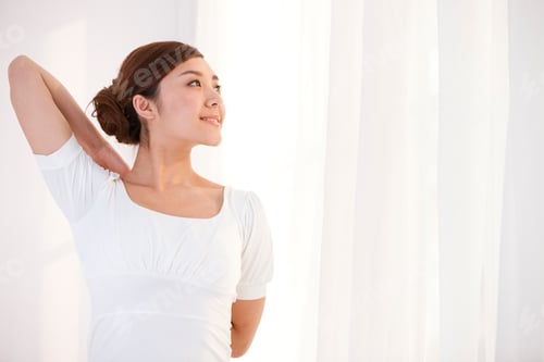 Preview: Young woman stretching and looking calm by the window