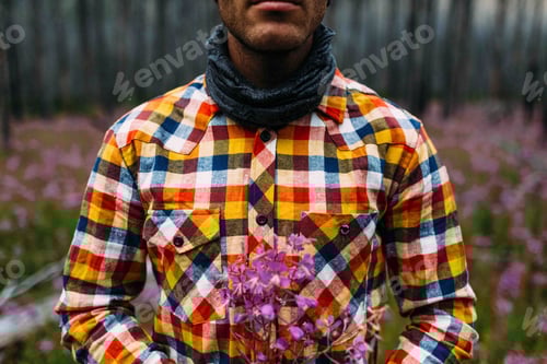 Preview: Man in a checkered shirt holding purple flowers in a field