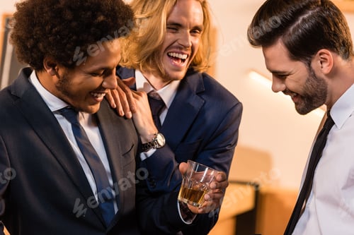 Preview: three multiethnic businessmen laughing while drinking whiskey in bar