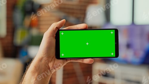 Preview: Holding Smartphone with Green Screen in Home Setting