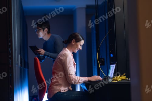 Preview: Caucasian female engineer using laptop and asian male engineer inspecting in computer server room