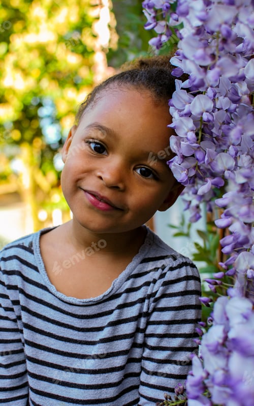 Preview: Portrait of a toddler girl in front of purple wisteria flowers - petals pink mixed race diversity