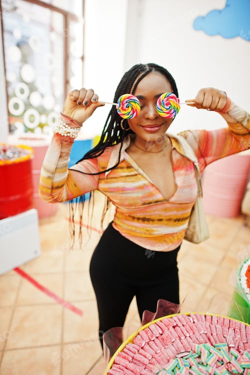 Preview: African american millennial lady at candy shop with lolipops.
