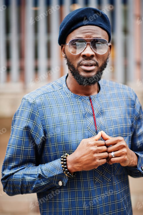 Preview: African guy in blue authentic costume, eyeglasses and beret. Fashionable nigerian man.