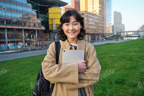 Preview: Happy asian girl stands on street, university student walks with digital tablet in hands and smiles