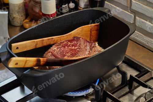Preview: Piece of meat is fried with onions in wine sauce in rectangular pan over fire on gas stove.