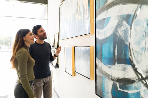 Preview: Smiling couple is looking at the paintings that are for sale at an art exhibition