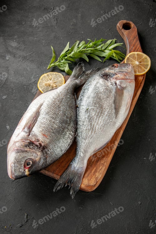 Preview: bottom view raw sea fish lemon slices on chopping board on black background