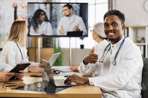 Preview: African american male physician with stethoscope working on laptop during online conference