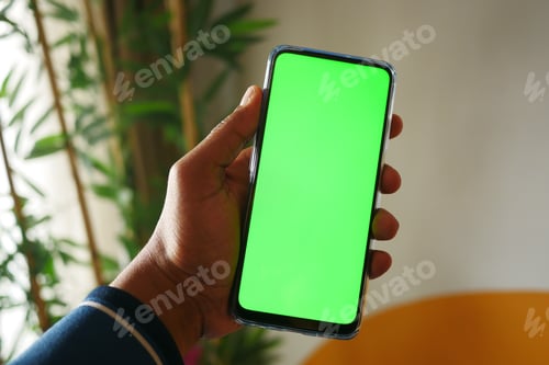 Preview: holding smart phone with green screen and home interior decoration on table