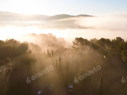 Preview: View of a misty landscape with trees and a building at sunrise in Aix-en-Provence, France.