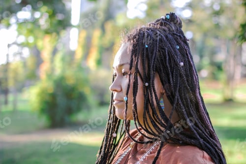 Preview: Portrait of beautiful European woman with long African braids and ethnic decorations in a park.