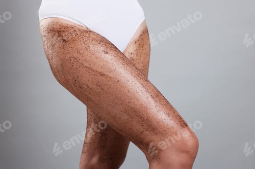 Preview: Woman with body scrub on her legs against grey background, closeup