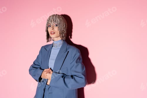Preview: Trendy young woman in jewelry headwear and blazer posing on pink background with shadow
