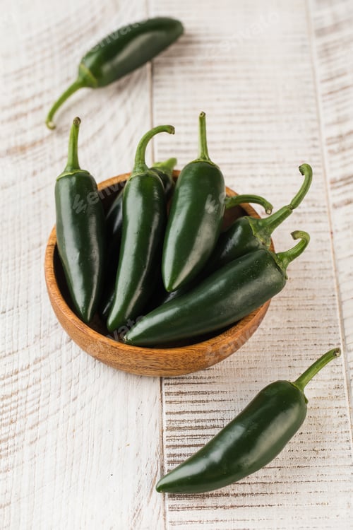 Preview: Green jalapeno peppers in a wooden bowl on a wooden background.