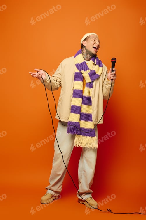 Preview: A young man with tattoos entertains on stage with a microphone against a bold orange background