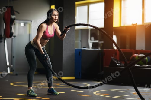 Preview: Athletic young woman doing crossfit exercises with a rope.