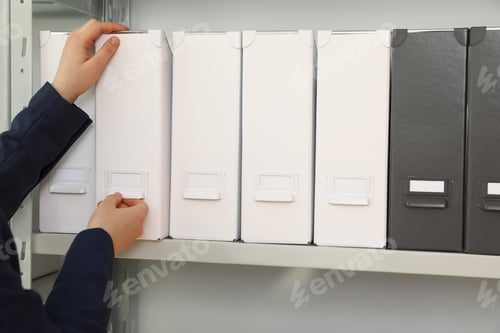 Preview: Woman taking folder with documents from shelf in archive, closeup