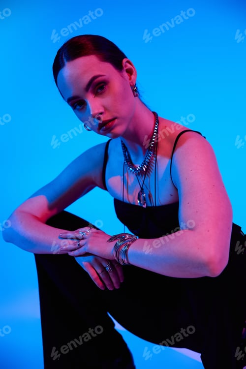 Preview: Young woman poses stylishly in studio with vibrant blue and pink lighting