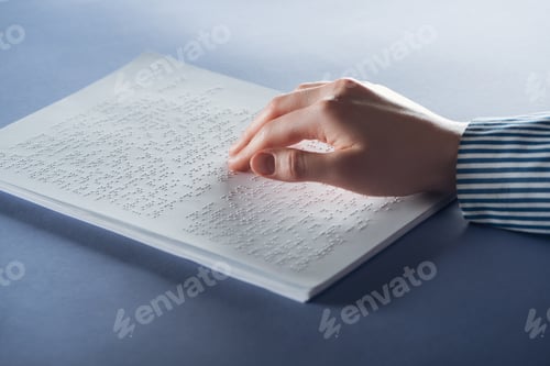 Preview: cropped view of young woman reading braille text with hand on blue