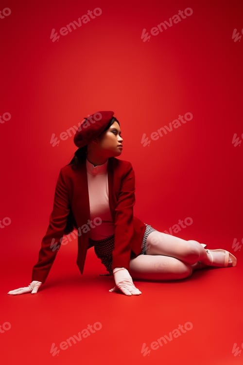 Preview: Pretty young asian model in stylish outfit sitting on red background