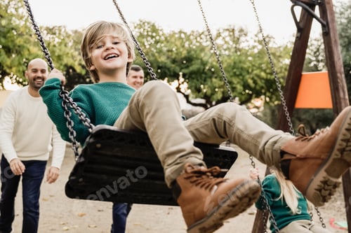 Preview: LGBT family - Happy children sons and fathers having fun swinging on swing at city park