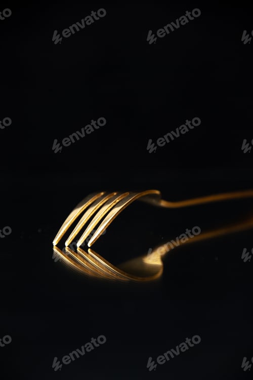 Preview: Vertical view of shiny golden fork put upside down on black background with free space