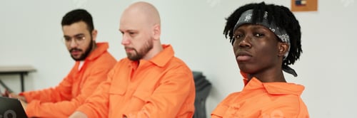 Preview: Young Multiethnic Men Wearing Orange Uniforms Sitting Indoors Working Together