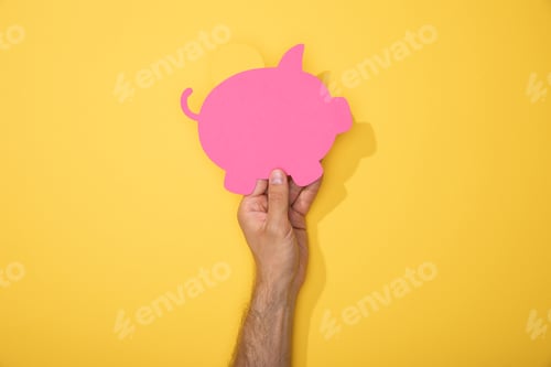 Preview: cropped view of man holding paper icon of pink piggy bank on yellow