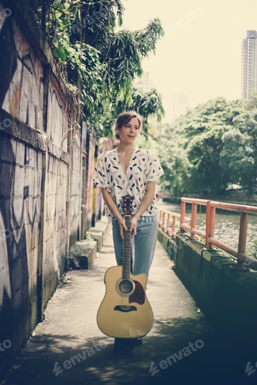 Preview: Young caucasian woman with a guitar outside