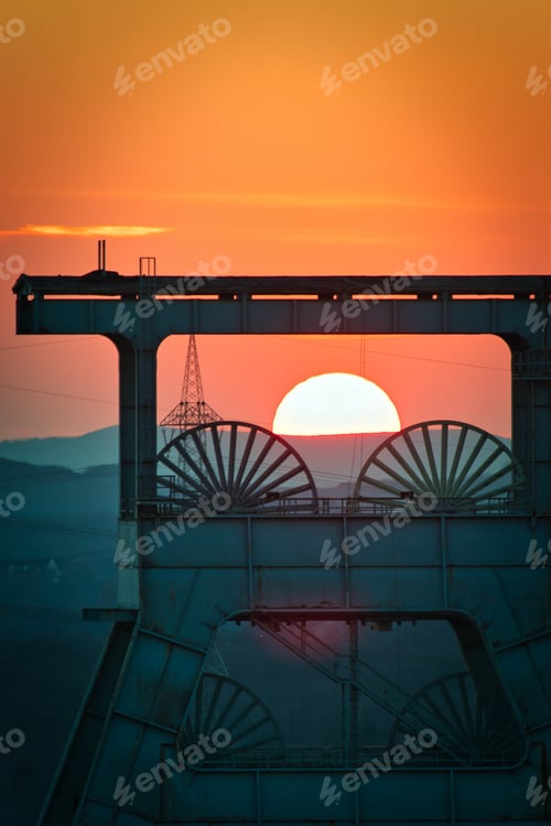 Preview: Vertical shot of a headframe tower with a golden sun setting in the background in Herten, Germany